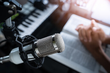 Microphone on desk with person praying, preacher reads the bible online, Christian podcast studio interior, records a podcast, online radio broadcast.