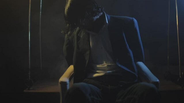 Cinema-like HD stock footage of a man tied to a chair in a dark mysterious room with creative dramatic lighting and some smoke element. HD - 24 Fps - Prores
