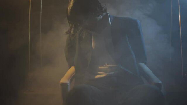 Cinema-like HD stock footage of a man tied to a chair in a dark mysterious room with creative dramatic lighting and some smoke element. HD - 24 Fps - Prores