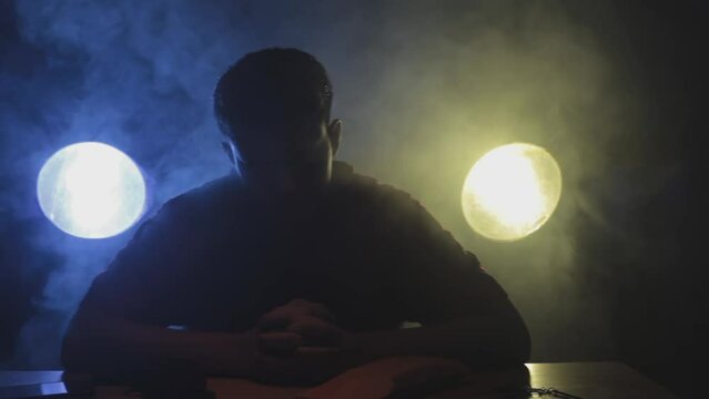 Filmic shot of a man in a red t-shirt sitting on a table preparing for a stealth mission packing his weapons and knives. Cinematic Full HD stock footage in ProRes.