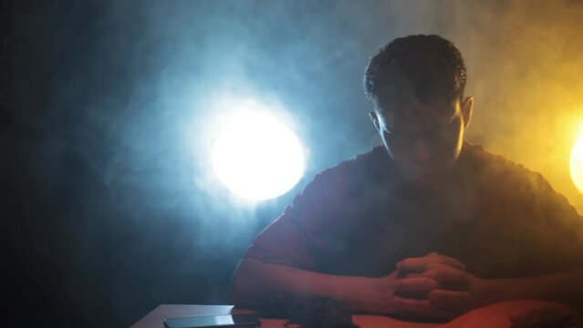 Filmic shot of a man in a red t-shirt sitting on a table preparing for a stealth mission packing his weapons and knives. Cinematic Full HD stock footage in ProRes.