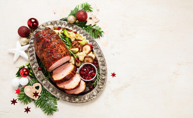 Roasted sliced Christmas ham on plate with vegetables, festive decoration.