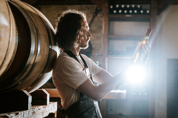 Winemaker tasting wine in a cellar with wooden barrels
