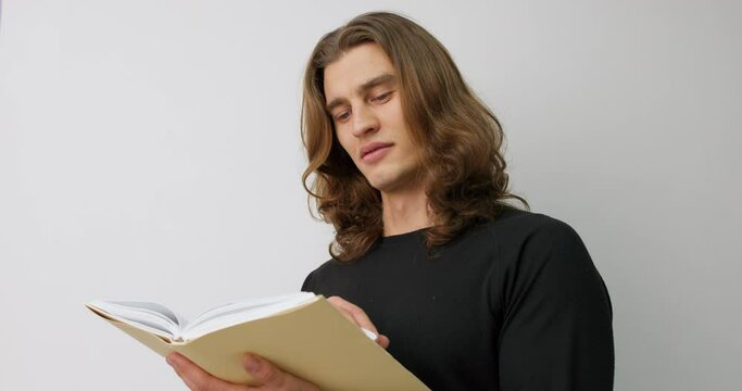 young serious clever man with lon hair concentrated on reading book free time Spare time Lifestyle student prepares for exams Slow motion Education Knowledge Guy gets information, look for information