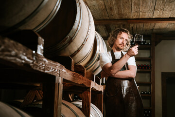 Fototapeta na wymiar Winemaker tasting wine in a cellar with wooden barrels