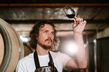 Winemaker tasting wine in a cellar with wooden barrels