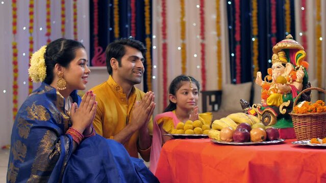 A nuclear Indian family in ethnic dress - praying on the occasion of Ganesh Chaturthi  Indian festival. Loving Indian family worshipping Lord Ganesha with puja ki thali - festival celebration  Indi...