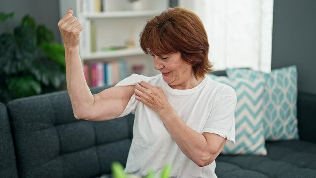 Middle age woman smiling confident doing strong gesture with arm home