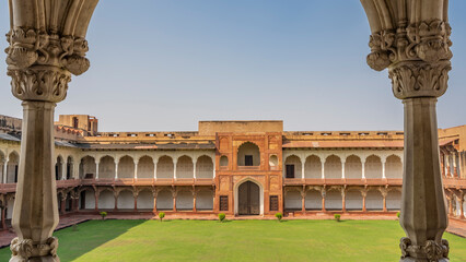 The courtyard in the Macchi Bhawan Palace of the Red Fort. Green grass on the lawn.  Along the perimeter there are galleries with columns, carved arches. In the center there is a balcony, a gate.
