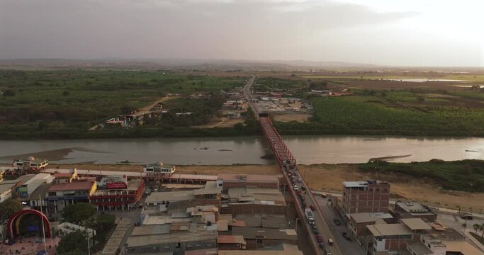 Aerial shot of Tumbes river, bridge and city at sunset. Tropical city at north of Per&uacute;. 