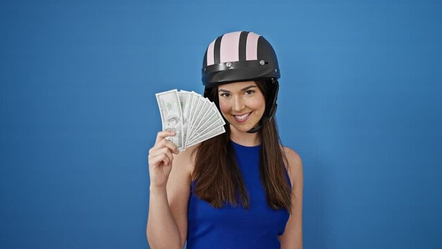 Young beautiful hispanic woman wearing motorcycle helmet holding dollars over isolated blue background
