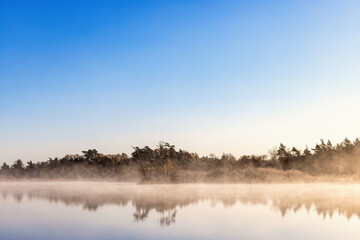 Beautiful autumn morning by a forest lake with fog