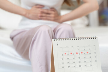 Close-up woman feeling stomach pain from cycle period on the bed at home.