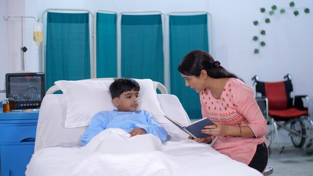 A Middle-aged Indian Woman Is Reading A Story Book To Her Sick Son In Hospital - Medical Problem. An Adorable Kid / An Indian Child Is Resting In The Hospital Room - Medical Facilities  Oxygen Nasa...