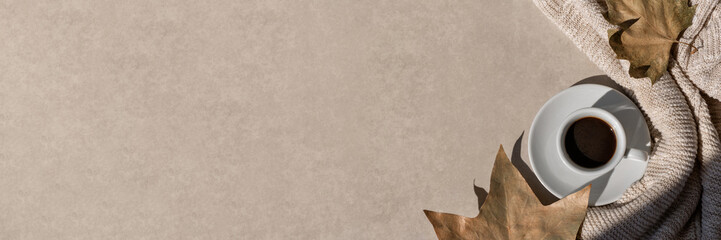 Coffee cup with hot drink, knitted cloth, light brown fall leaves on neutral beige background....