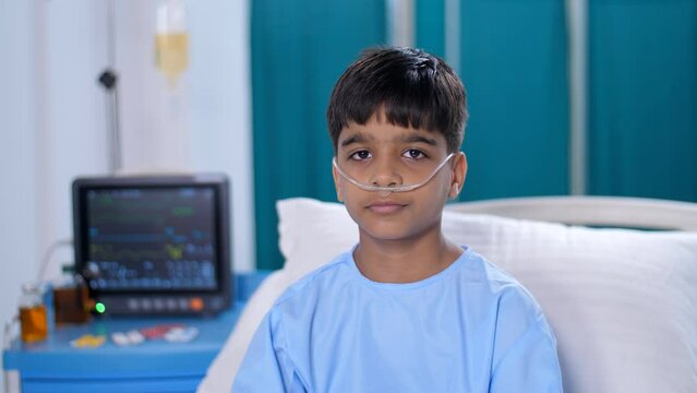 A five-year-old kid with an oxygen nasal tube is posing for the camera - hospital care. A sweet boy wearing a hospital gown is admitted to the hospital - a sick patient  a medical problem  medical ...