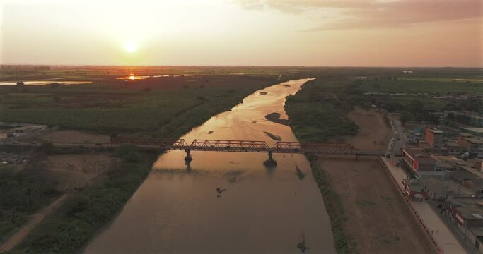Aerial shot of Tumbes river, bridge and city at sunset. Tropical city at north of Per&uacute;. 