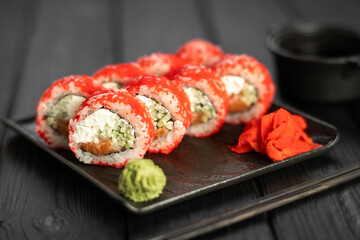 California sushi roll with crab, cucumber and tobiko caviar served on a black plate with wasabi and ginger on wooden table. Isolation on a black background. Japanese food