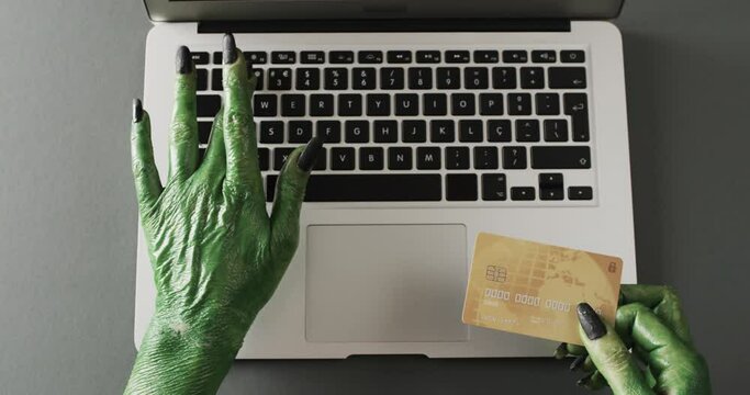 Video of halloween green monster hands holding card and laptop with copy space on grey background