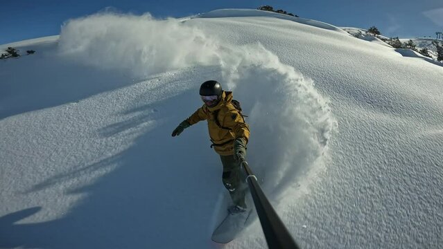 Snowboard freeride skiing in resort, active man 40 years old enjoying fresh snow doing powderterns snowboarding in powder day, filming selfie stick. Adrenaline junkie gets his fill from snowboarding