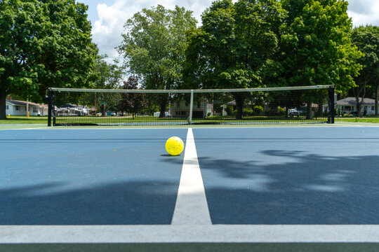 Recreational sport of pickleball court and ball in the United States with green and blue court with yellow ball on line.