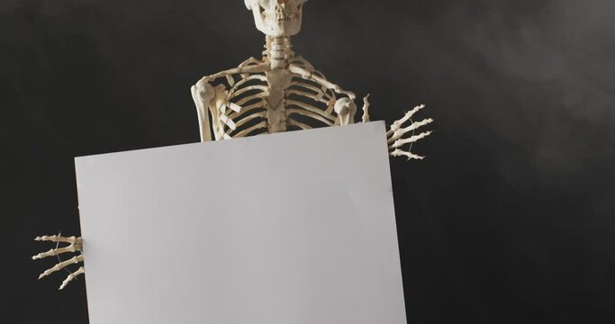 Video of close up of halloween skeleton holding white board with copy space on black background