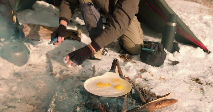 Hicker Cooking Eggs Over Firewood. Winter Outdoor. young man frying eggs for breakfast resting on sunny cold day Slow motion