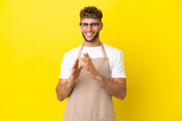 Restaurant waiter blonde man isolated on yellow background applauding after presentation in a conference