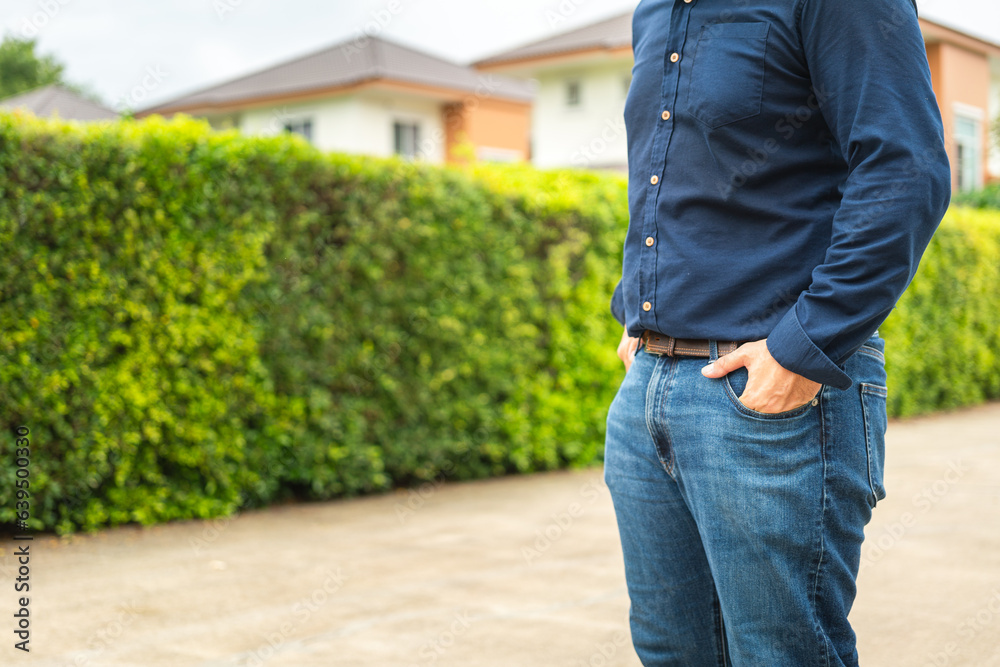 Poster A man in blue long sleeve shirt is standing with confident action on blurred background of luxury house. Successful business man concept scene, close-up and selective focus.