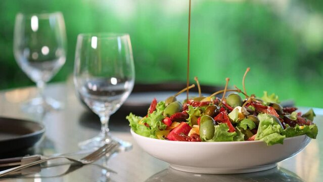 Healthy salad with sun-dried tomatoes, mozzarella cheese, greens, capers and olives. Dressing fresh salad with balsamic vinegar. Healthy food concept. Pouring olive oil on the vegan salad