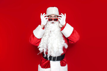 shocked santa claus in red glasses looks at the camera in surprise and is amazed on colored background