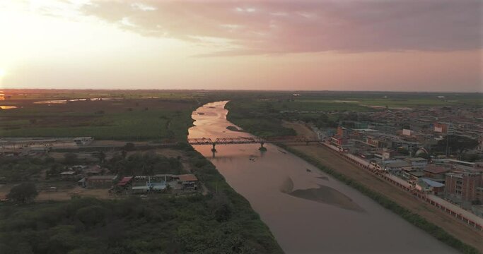 Aerial shot of Tumbes river, bridge and city at sunset. Tropical city at north of Per&uacute;. 