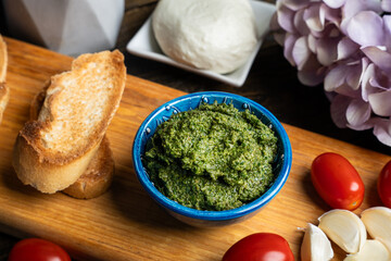 Traditional Italian pesto sauce served with mozzarella cheese, tomatoes and bruschetta on a dark wooden table