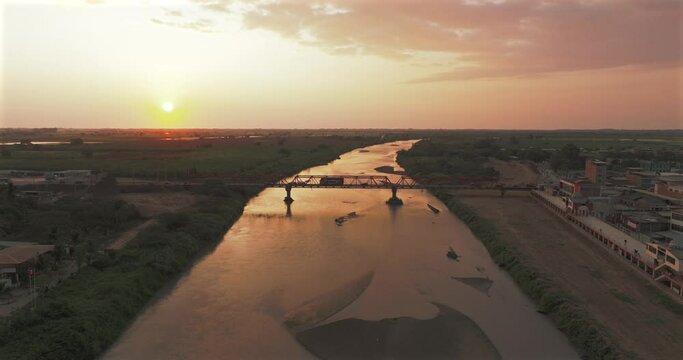 Aerial shot of Tumbes river, bridge and city at sunset. Tropical city at north of Per&uacute;. 