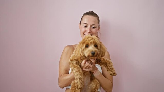 Young caucasian woman with dog smiling hugging over isolated pink background
