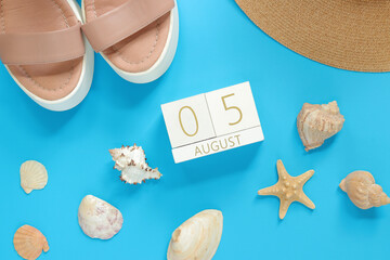 August 05. Wooden calendar on a blue background with summer accessories, top view. Vacation in summer. Perpetual calendar, boots, hat and shells with starfish