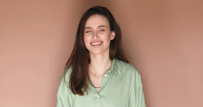 Lovely coquettish brunette woman, look playfully, flirting, fix her hair. Woman fix her hair isolated on beige background, look happy. Brunette hair fashion model face smiling. Girl wear green shirt.