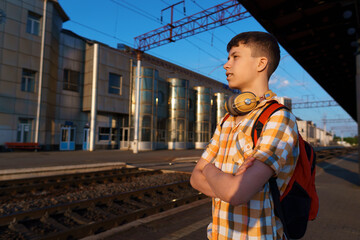 a student poses at a railway station, a teenage boy walks along the platform to the train, he has a backpack and books, goes to study, the concept of education