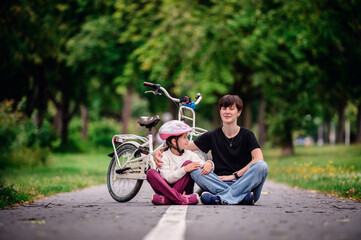 Obraz premium Young mother in jeans and black t-shirt teaching and sitting with her daughter on track in summer parks while speaking