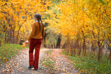 Fototapeta premium a young teenage girl walks in the autumn forest, goes along the road and enjoys the beautiful nature and bright yellow leaves