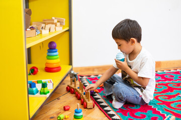 Boy playing with wooden train toy in kindergarten