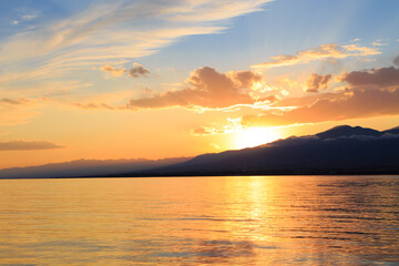 Colorful sunset on the sea. Mountain lake in the rays of the orange sun. Kyrgyzstan, Lake Issyk-Kul.