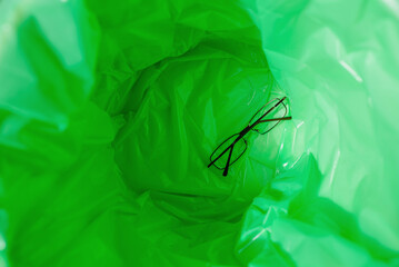A green garbage bag in the trash. There is an eyeglasses inside.Top view.