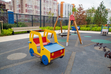 Rocking chair on a yellow and blue metal spring made of natural wood in the shape of a car on a playground on a clear sunny day. Kids sports hobbies.