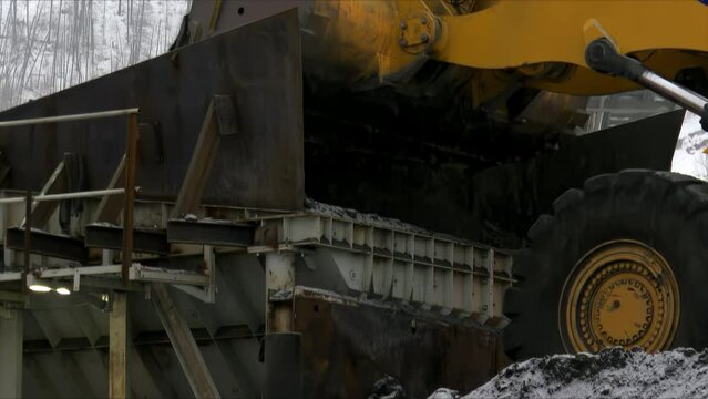 Close-up of a grader dumping ore onto a protractor belt in heavy snowfall.