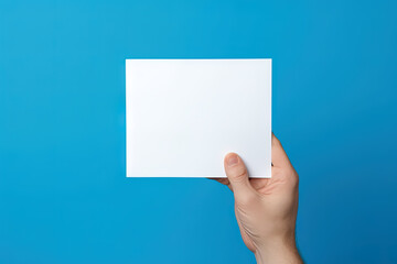 A human hand holding a blank sheet of white paper or card isolated on blue background