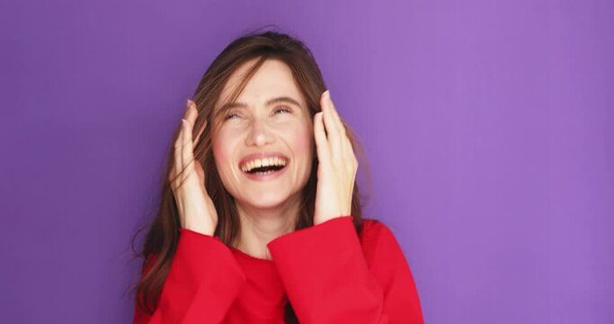 Positive smiling young woman peeking through fingers with curious nosy expression, spying secret information standing on purple background. She open face and laughing. Girl look happy.