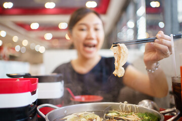 Happy - cheerful Asian fat woman enjoy eating a traditional Asian Hotpot or Sukiyaki in the Asian...