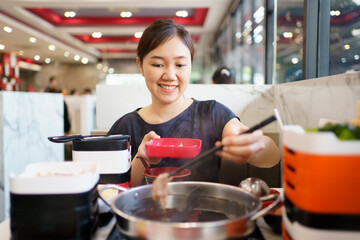 Happy - cheerful Asian fat woman enjoy eating a traditional Asian Hotpot or Sukiyaki in the Asian Hotpot restaurant.