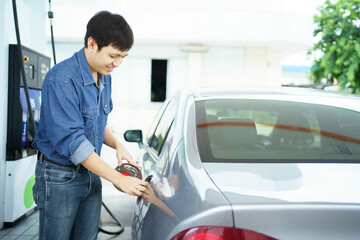 Happy cheerful Asian middle adult man refueling his car at self-service gas station.
